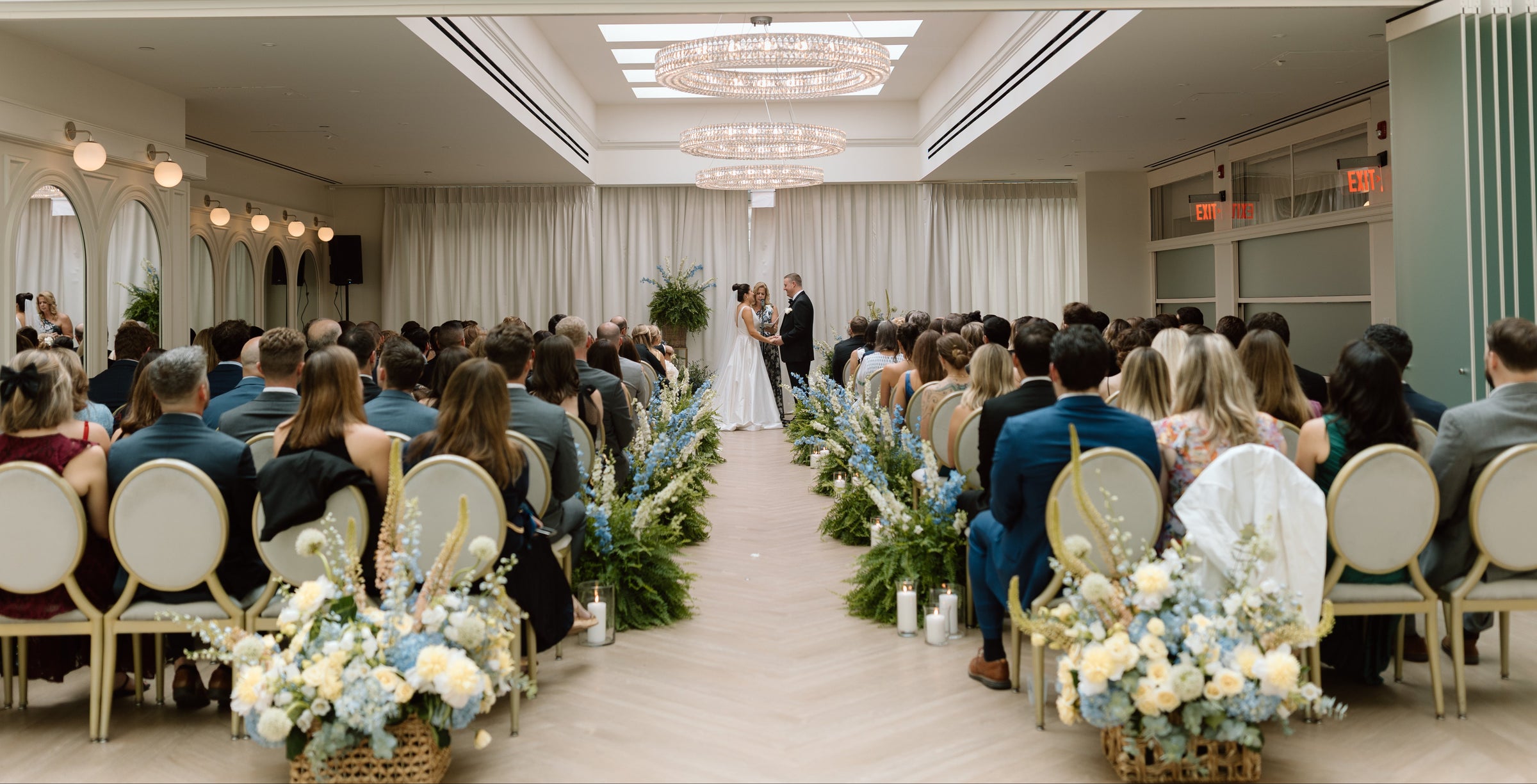 Wedding ceremony in a large, well-lit indoor venue with floral decorations.